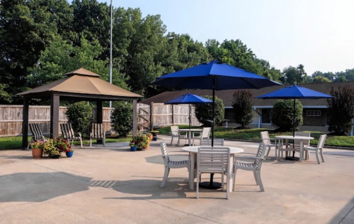 A serene outdoor patio with tables, chairs, and umbrellas surrounded by greenery.