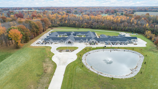 Aerial view of a modern building surrounded by landscaped grounds and a pond, showcasing vibrant autumn colors.