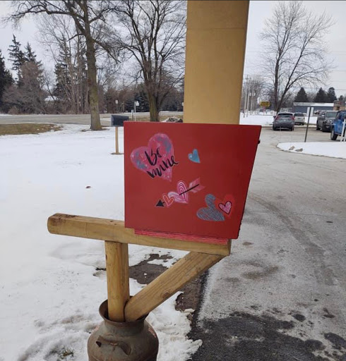 A creatively decorated red mailbox with heart motifs, standing in a snowy landscape.