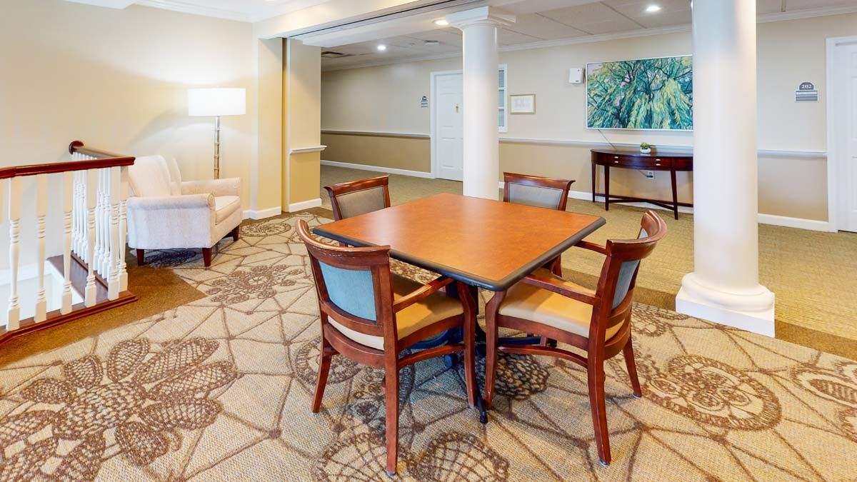 A cozy seating area in an indoor space featuring a wooden table and four chairs on a patterned carpet.