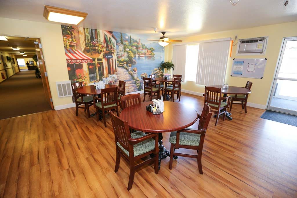 A cozy dining area featuring wooden floors, round tables with chairs, and a scenic mural on the wall.
