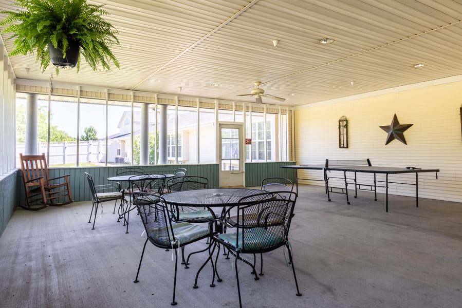A bright indoor seating area with metal tables and chairs, surrounded by large glass windows allowing natural light to fill the space.