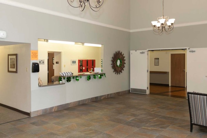 A spacious lobby area featuring a reception window, decorative mirror, and chandelier lighting.