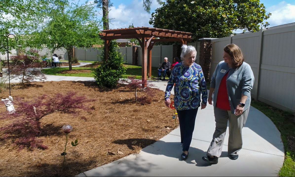Two people walking along a garden pathway on a sunny day.