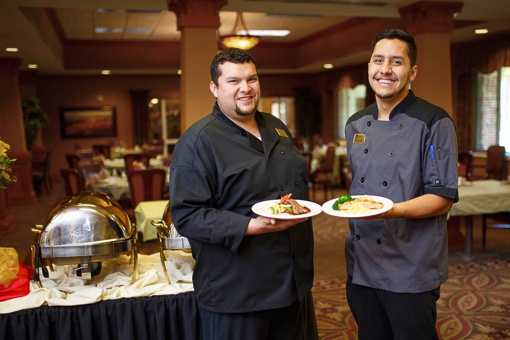 Two chefs proudly display their culinary creations in a restaurant setting.