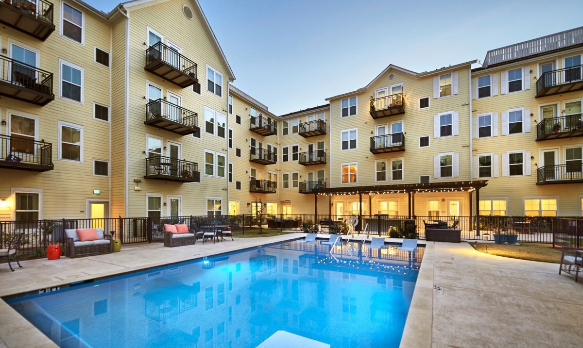 A modern apartment complex featuring an illuminated outdoor pool area during the evening.