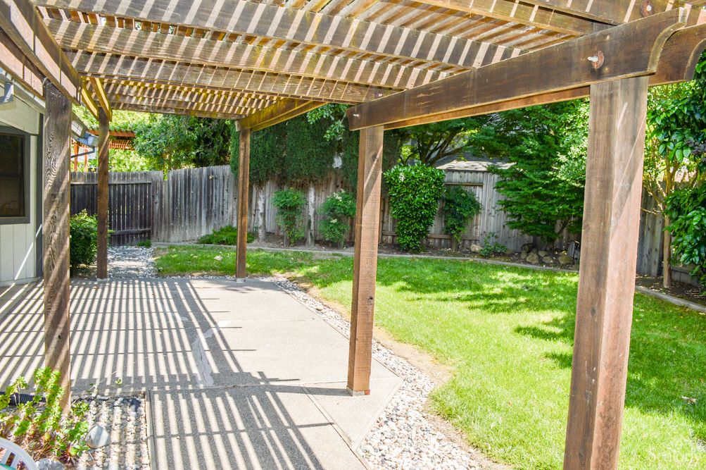 A tranquil backyard with a pergola casting shadows over the patio and lush green lawn.