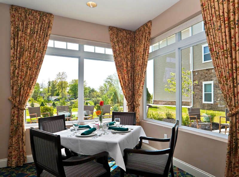 A cozy dining area with a beautifully set table, surrounded by large windows that offer a bright and scenic view.