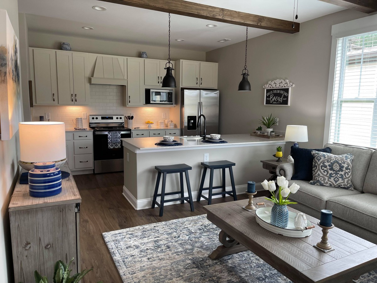A modern open-concept kitchen and living area featuring cozy decor with pendant lighting, bar stools, and a wooden floor.