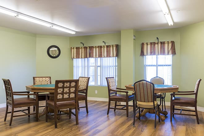 A cozy dining area with tables and chairs, featuring large windows and a wooden floor.