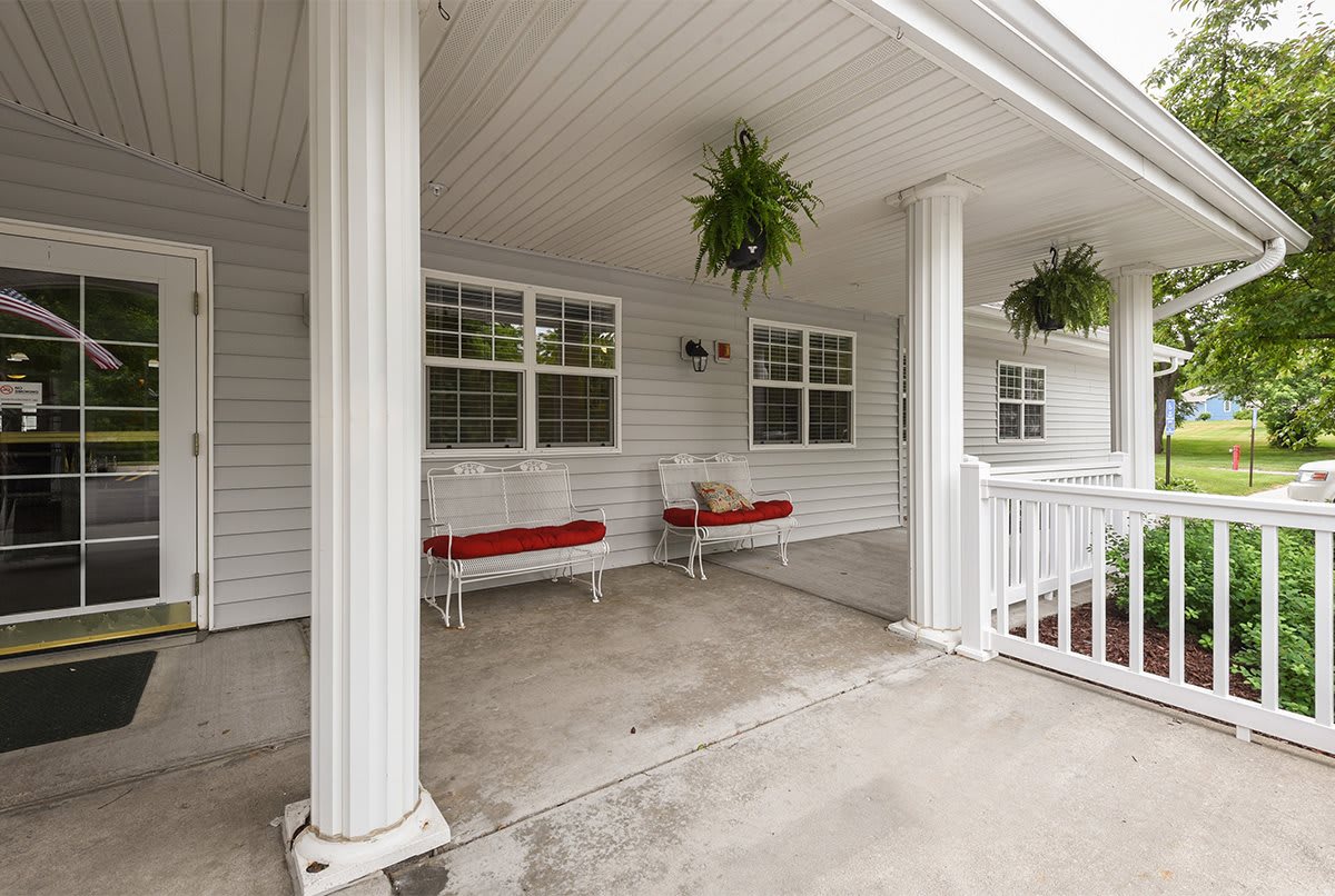 A cozy porch with white columns, hanging plants, and red-cushioned benches.
