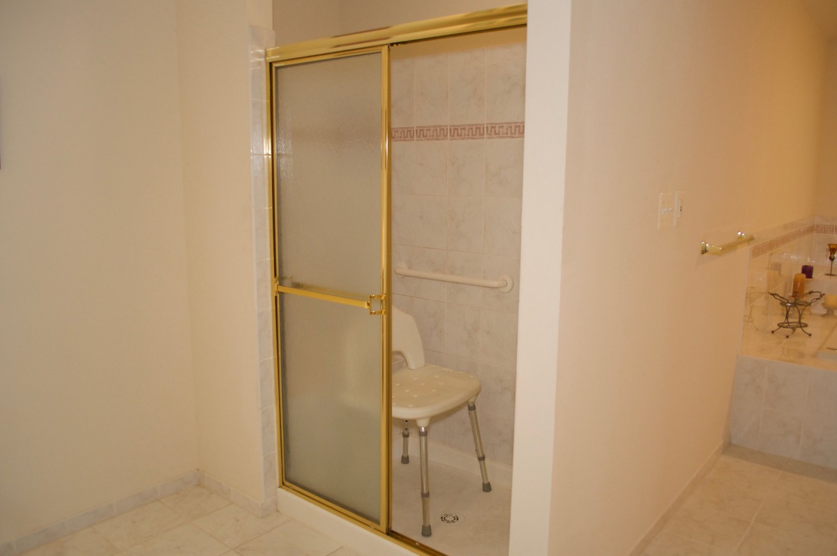 A bathroom shower with a gold-framed sliding door and a chair inside.