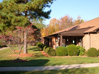 A suburban house surrounded by trees and a well-maintained lawn on a sunny autumn day.