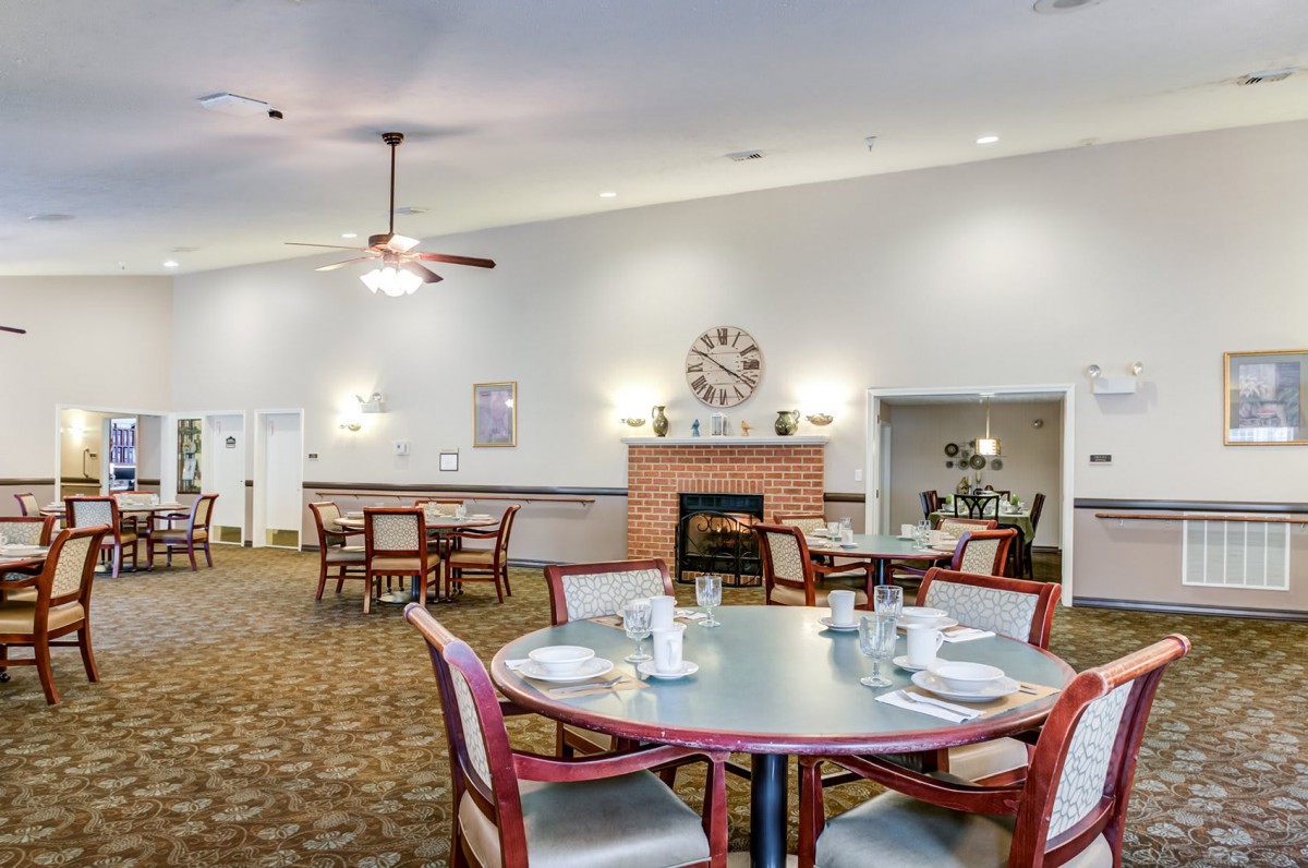 A well-arranged dining room with tables and chairs, featuring a fireplace and wall clock.