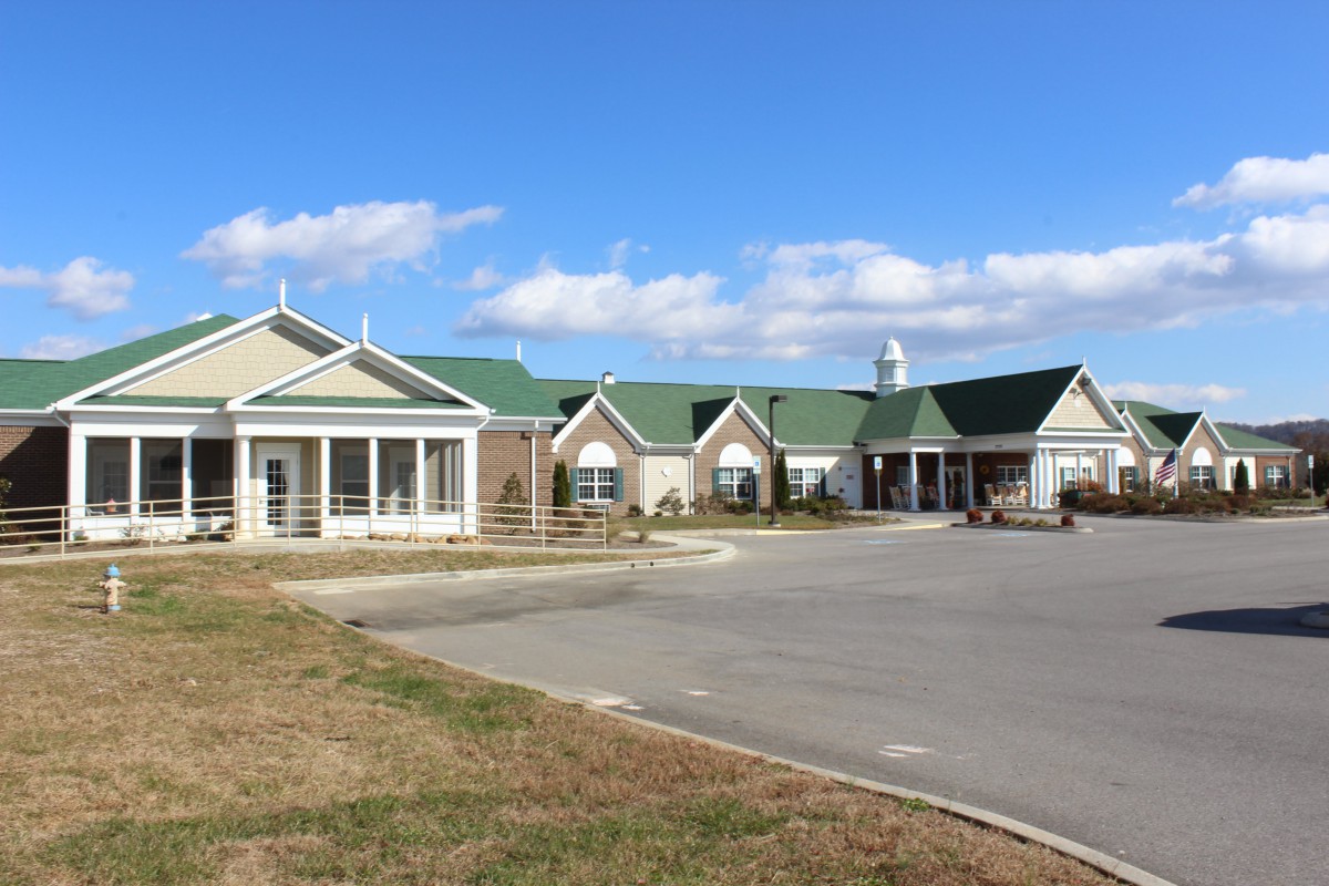 A view of a building with a green roof and parking lot under a clear sky.