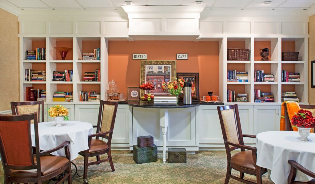 A cozy library interior with bookshelves, a coffee station, and seating area.