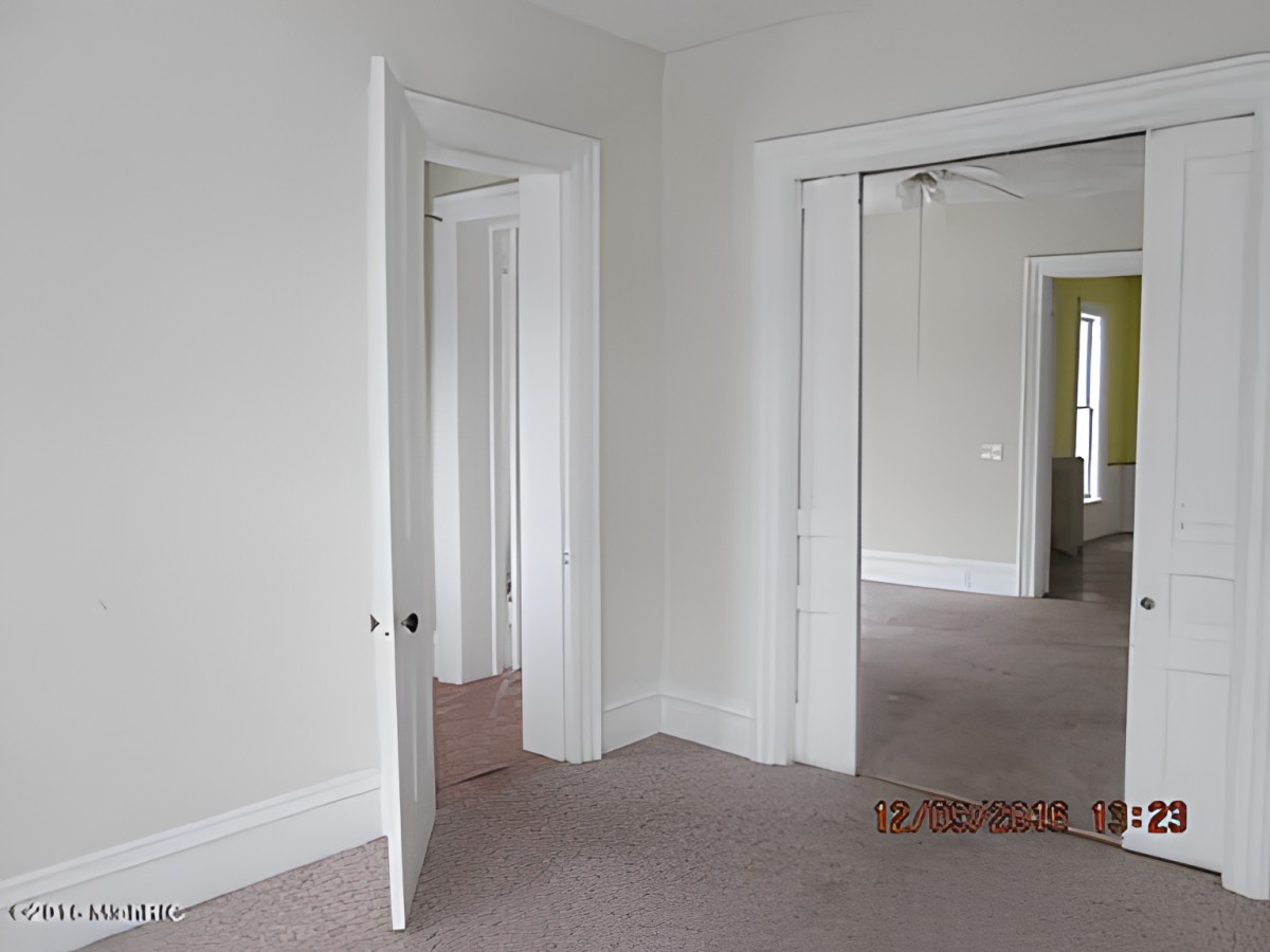 An empty room with white walls, carpeted floors, and multiple doorways.