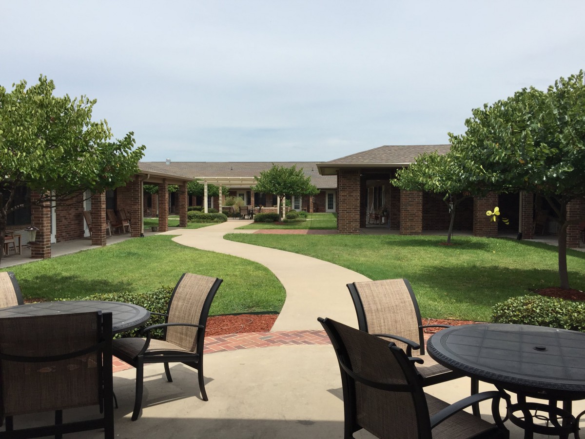 A peaceful courtyard with a winding pathway, surrounded by buildings and greenery, featuring outdoor seating arrangements.