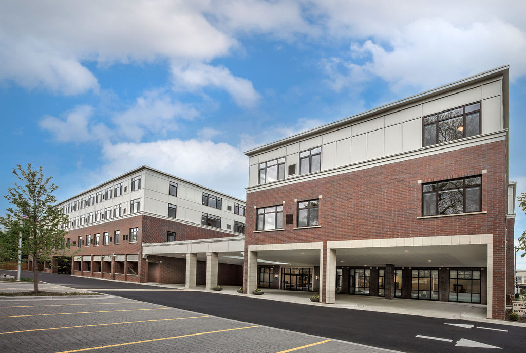 A modern school building with brick exterior and large windows under a partly cloudy sky.