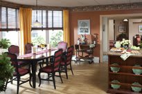 A cozy dining room with a wooden table and chairs, featuring large windows with yellow curtains.