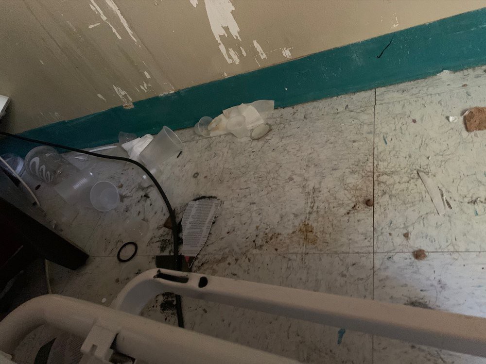 A room corner with a dirty floor, peeling paint, and scattered debris.