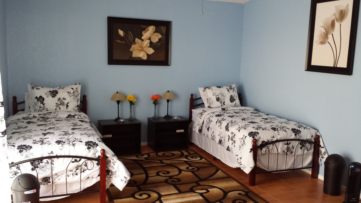 A cozy bedroom with two single beds adorned with floral bedding, flanked by matching nightstands and lamps against serene blue walls.