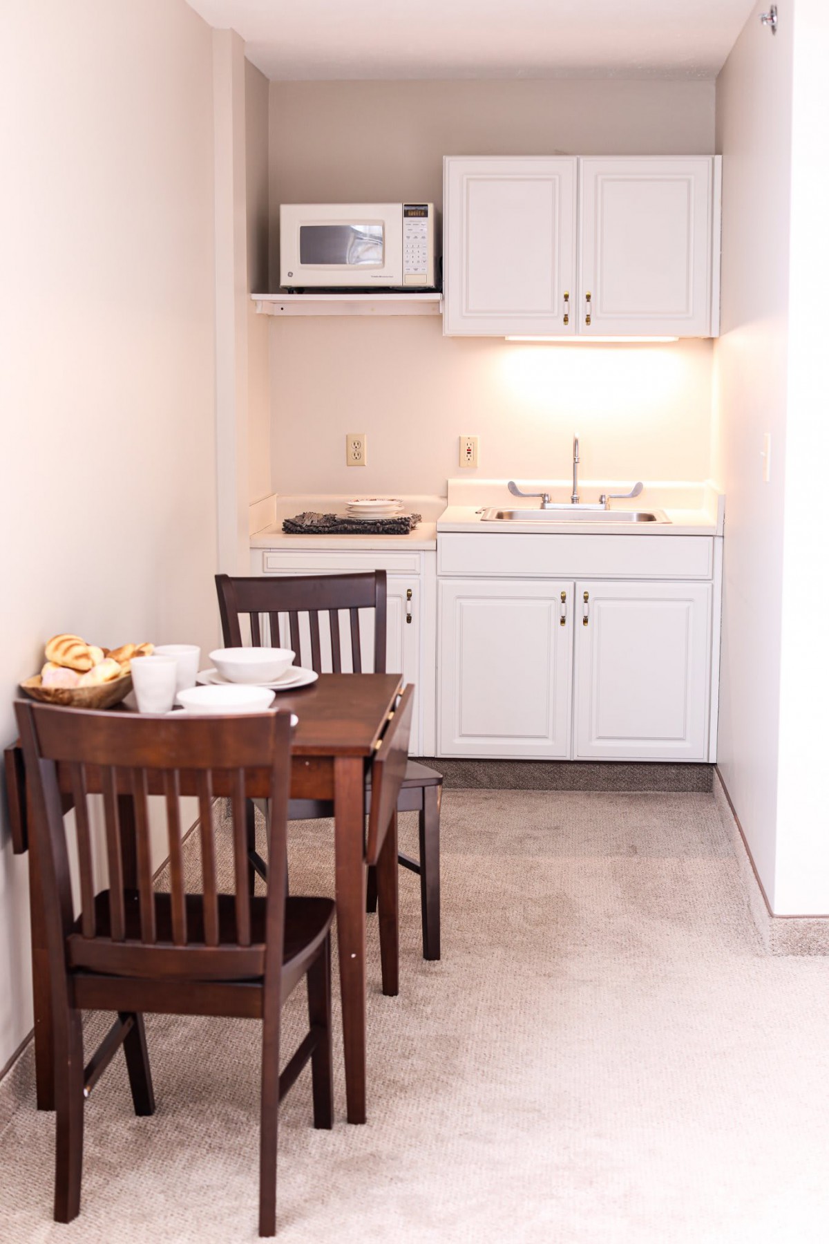 A compact kitchenette with a dining table and chairs, featuring a microwave, sink, and cabinetry.