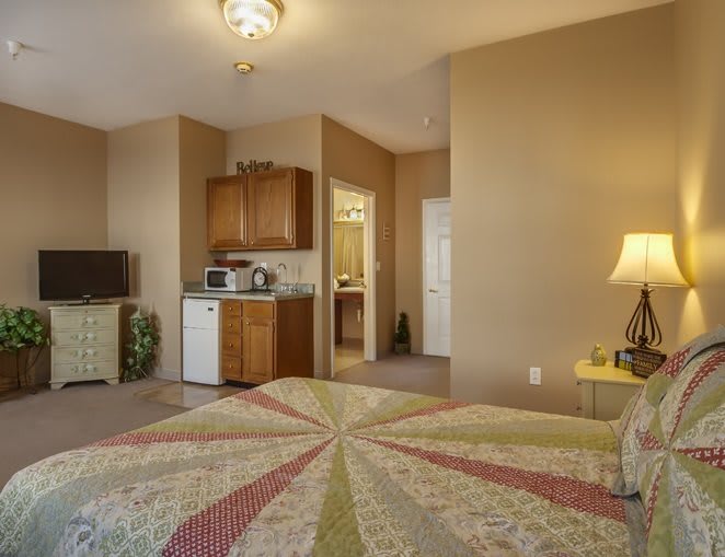 A cozy hotel room with a kitchenette, featuring a bed, television, and warm lighting.