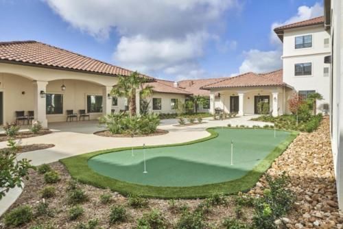 A spacious backyard with a putting green and lush landscaping under a cloudy sky.