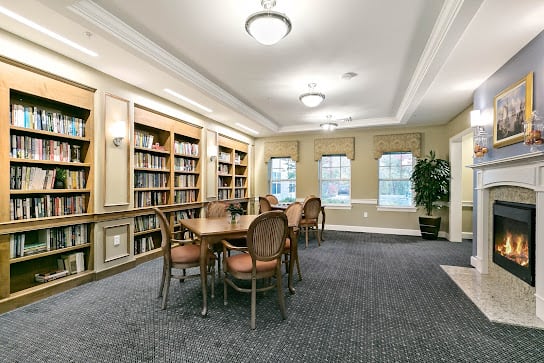 A cozy library reading room with bookshelves and a large table surrounded by chairs.