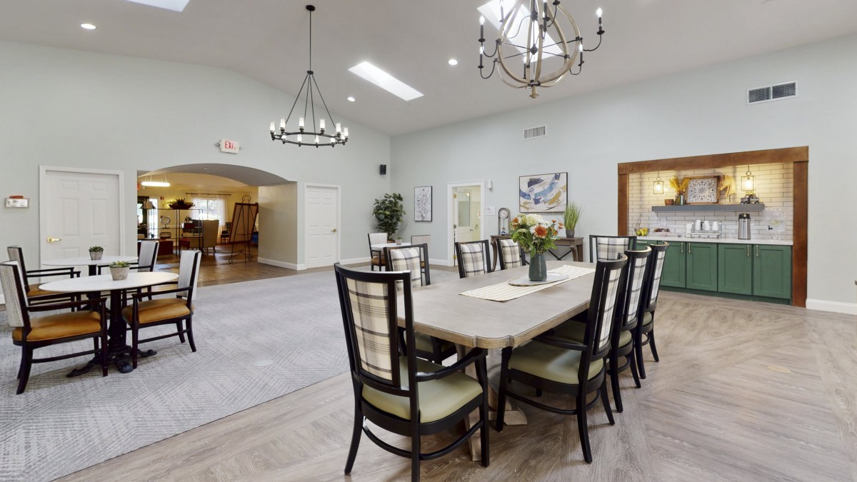 A spacious dining room featuring a large table, surrounded by chairs and illuminated by chandeliers.