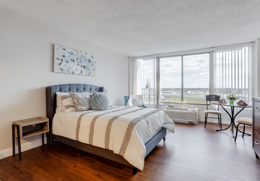 A modern bedroom with large windows, featuring a cozy bed and abundant natural light.