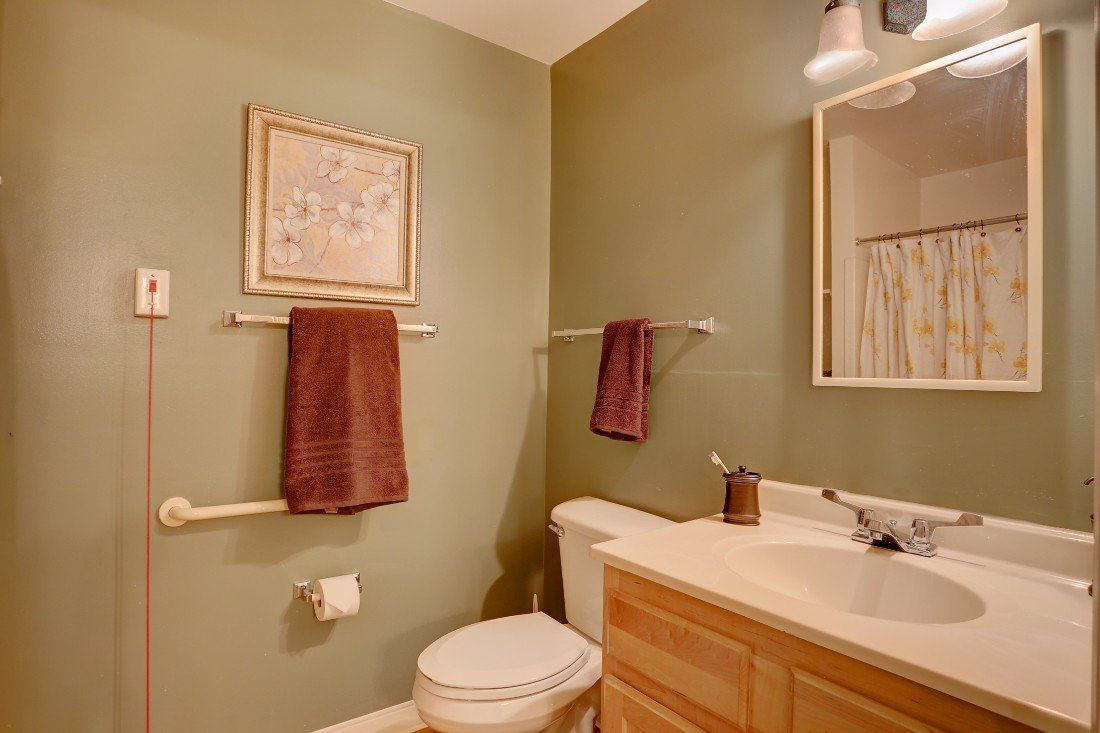 A cozy bathroom with green walls, featuring a sink, toilet, and brown towels.