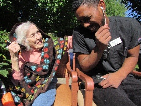 An elderly woman and a caregiver share a joyful moment outdoors.