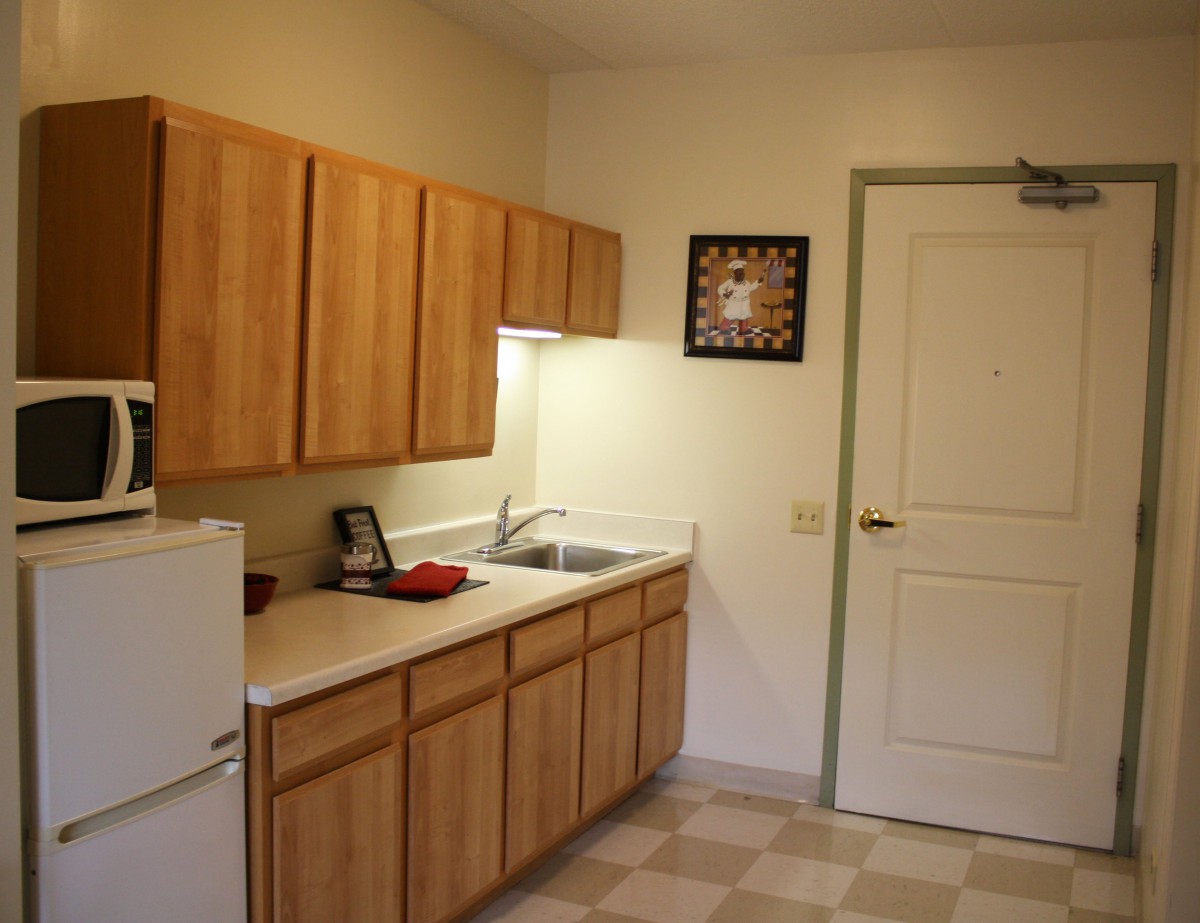 A simple kitchen with wooden cabinets, a refrigerator, and a sink.