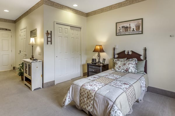 A cozy bedroom featuring a single bed with patterned bedding, a bedside table with a lamp, and wall art for decor.