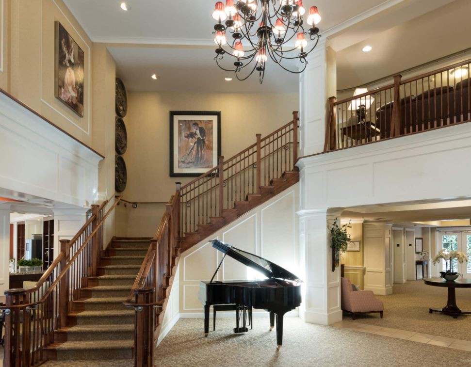 A luxurious lobby featuring a grand piano, elegant staircase, and chandelier.