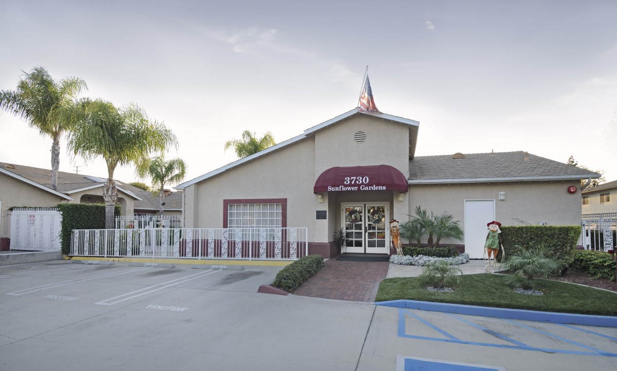 An office building entrance with an awning and adjacent parking lot, surrounded by palm trees.