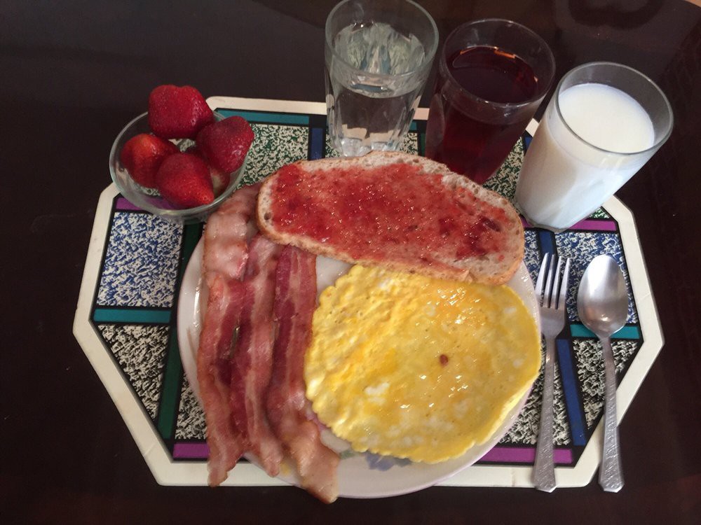 A hearty breakfast with bacon, eggs, toast with jam, strawberries, and drinks including milk, juice, and water.