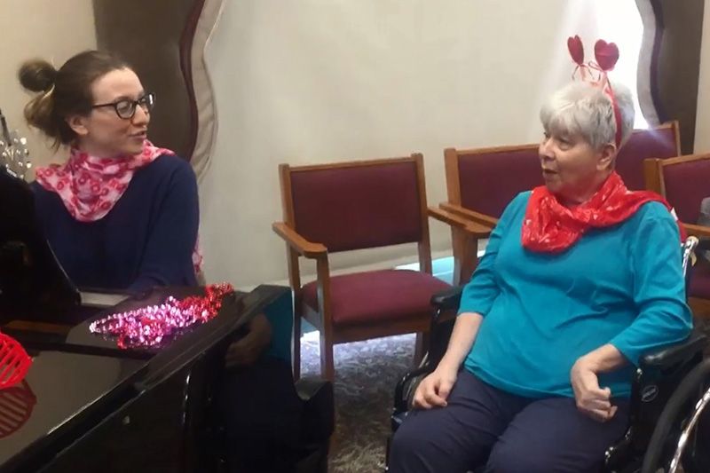 Two people having a conversation indoors, seated on chairs with festive decorations.