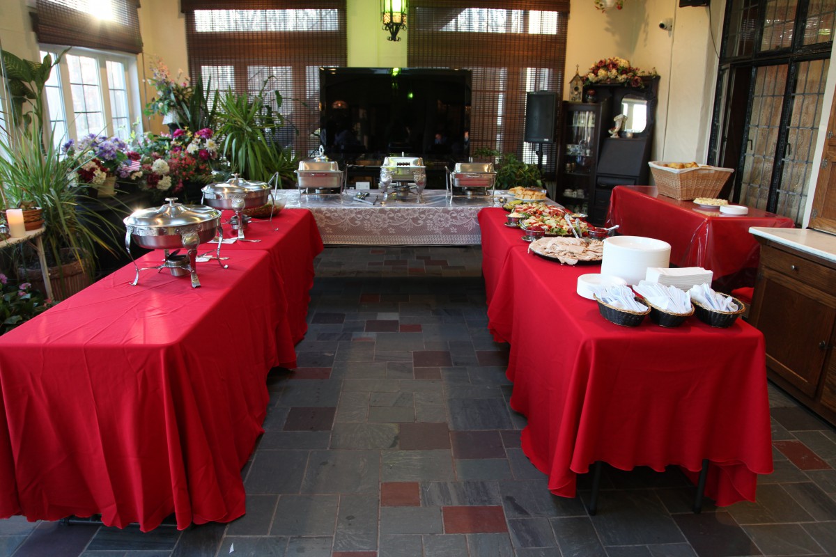 An indoor buffet setup with red tablecloths displaying a variety of food items on several tables.