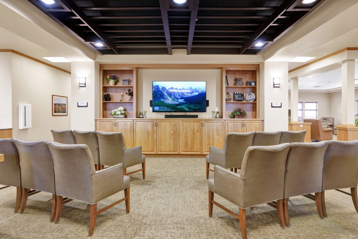 A cozy seating area with comfortable chairs facing a television, surrounded by wooden shelves and warm lighting.