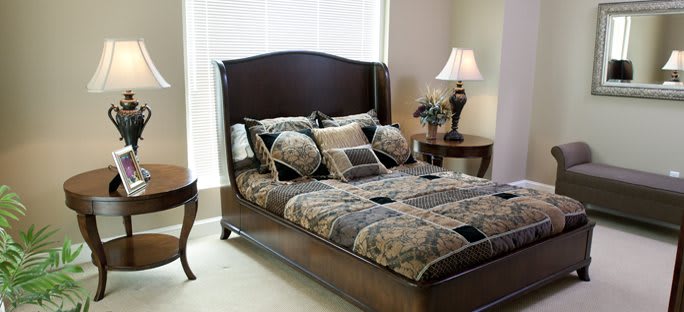 A well-decorated bedroom featuring a stylish bed with patterned bedding, a side table, and an elegant lamp.