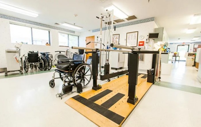 A rehabilitation room equipped with a wheelchair and parallel bars for physical therapy.
