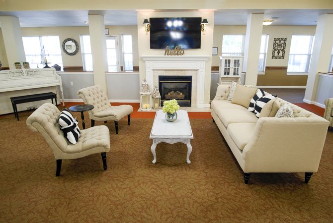 A cozy living room featuring a fireplace, sofa, armchairs, and a television mounted above the mantle.