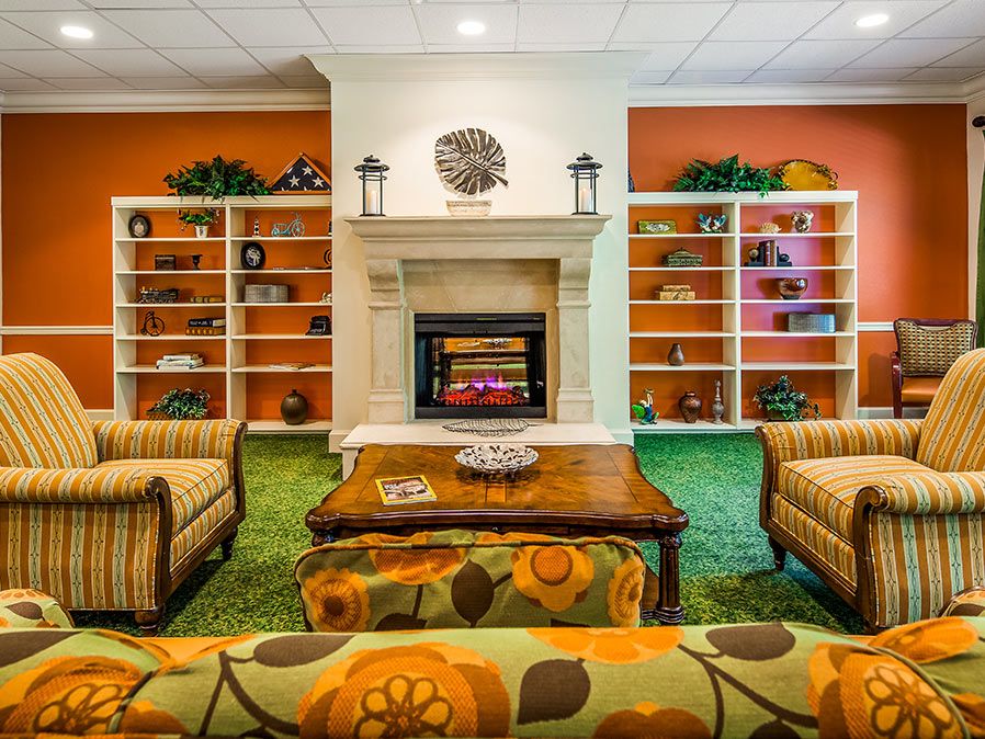A cozy living room with a central fireplace, surrounded by bookshelves and colorful furniture.