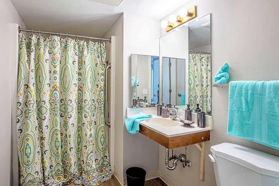 A clean and organized bathroom with a colorful shower curtain, a well-lit vanity area, and neatly arranged toiletries.