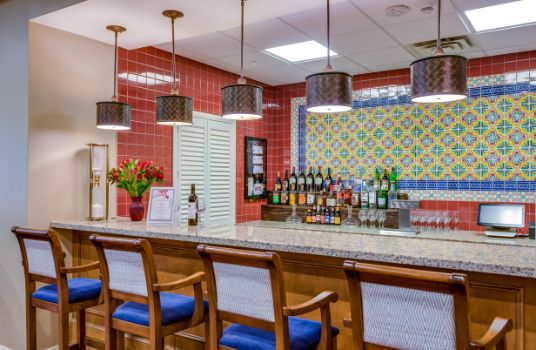 A stylish bar area with wooden seating, colorful tiled walls, and a variety of bottled drinks on display.