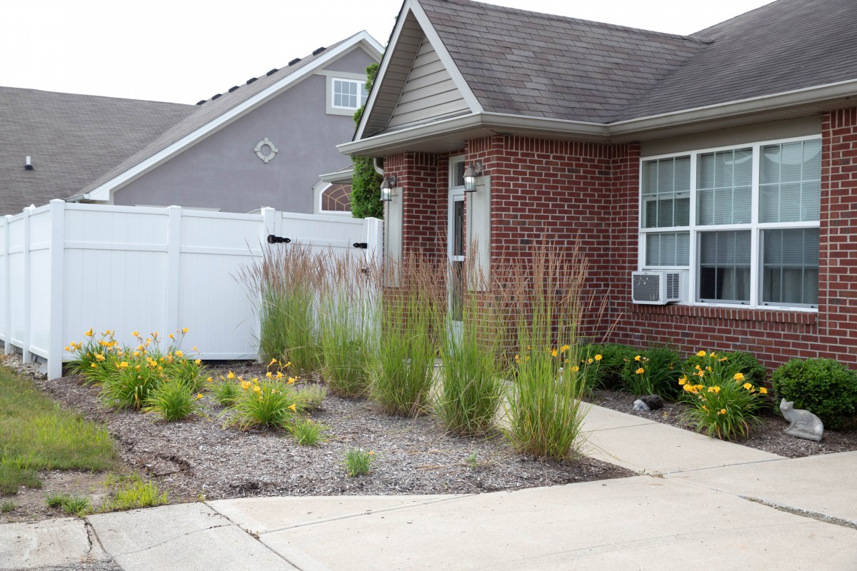 A brick house with a well-landscaped front yard featuring ornamental grasses and a paved driveway.