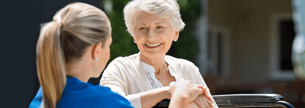 An elderly woman smiling while interacting with a caregiver outdoors.